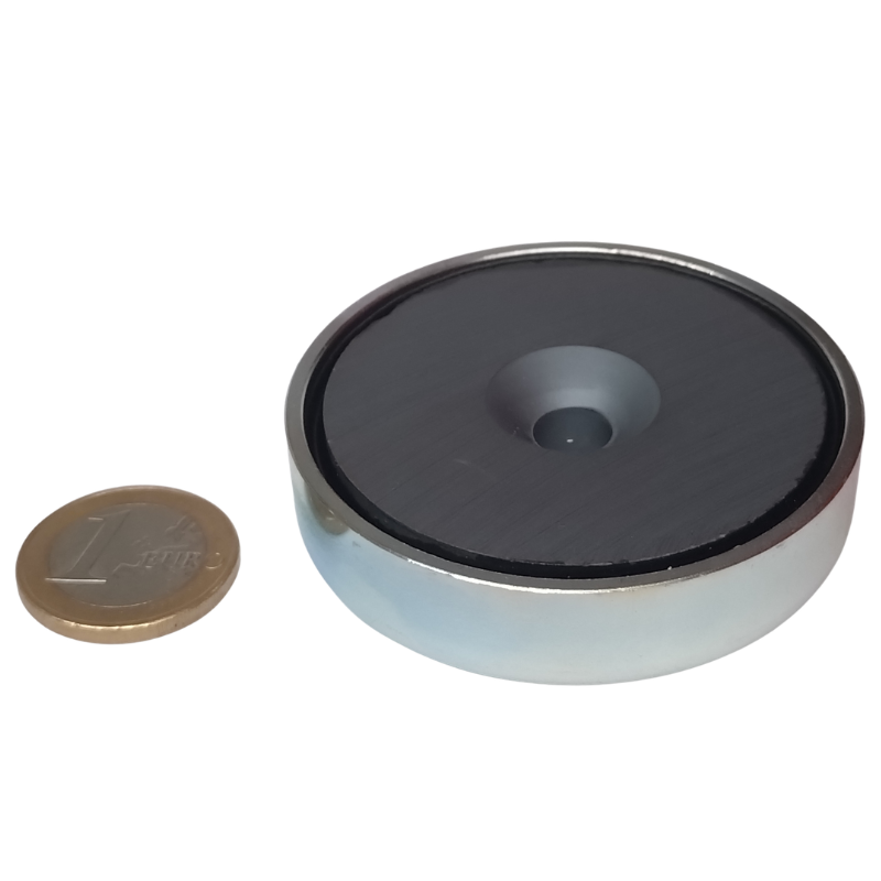 Een Keramische potmagneet met verzonken gat (25mm x 7mm, houdkracht 3kg) ligt naast een 1-euromunt, zodat je het formaat van de magneet goed kunt vergelijken.